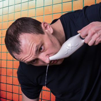 man cleans his nasal passages with a neti pot in the bathroom